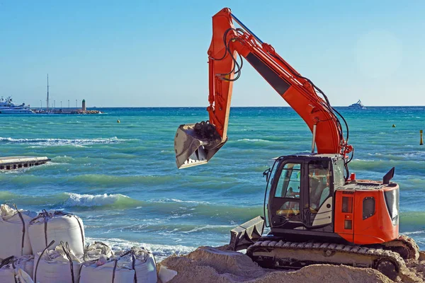Mavi denizin arka planına karşı Cannes Fransız kenti sahilde Turuncu ekskavatör. Sahili güçlendiriyor. Ünlü Croisette'i fırtına ve dalgalardan koruyun.