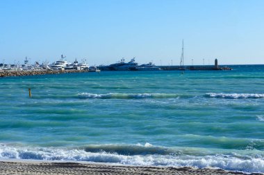 Turkuaz deniz, beyaz Yatlar, deniz feneri ve güneşli bir günde kum ayak izleri. Cannes, Fransa. Ünlü Croisette ve plaj.