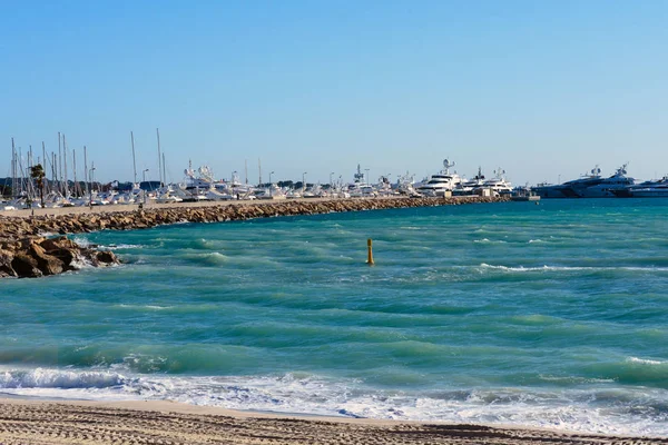 Turquoise zee, witte jachten, vuurtoren en voetafdrukken in het zand op een zonnige dag. Cannes, Frankrijk. De beroemde Croisette en het strand. — Stockfoto