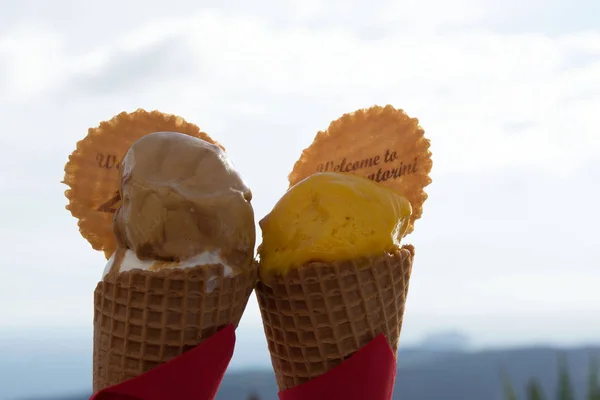 Heerlijke chocolade en mango ijs in wafel bekers tegen de achtergrond van de zee en de bergen. Eiland Santorini, Griekenland. Ijs smelt onder de stralen van de avondzon. Smakelijke reis. — Stockfoto