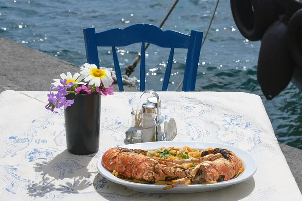 Delicious lunch by the sea. A white plate of spaghetti with huge lobsters on the grill. Travel to Santorini, Greece. Old port of Fira. Cozy family restaurant. Tasty trip.