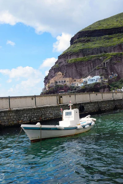 Santorini, Griekenland, april 2019. Een kleine witte vissersboot in de oude haven van de Griekse stad Fira. Boot op de achtergrond van bergen en de zee op een zonnige dag. Een interessante reis. — Stockfoto
