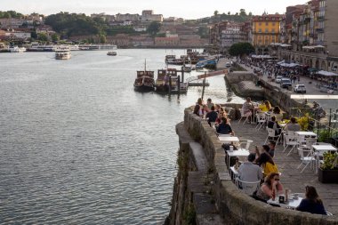 Porto, Portekiz, Haziran 2019. Gün batımında Douro Nehri'nin dolgusu. Turistler ve Porto sakinleri set boyunca yürüyüş, bir restoranda yemek, nehir üzerinde bir tekne binmek. Yolculuk.