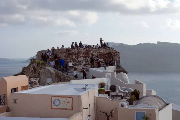 Santorini, Kreikka, huhtikuu 2019. Valkoinen perinteinen kreikkalainen taloa rinteellä saarella Santorini. Turistit odottavat auringonlaskua. Auringonlasku kaupungissa Oia, Santorini . — kuvapankkivalokuva