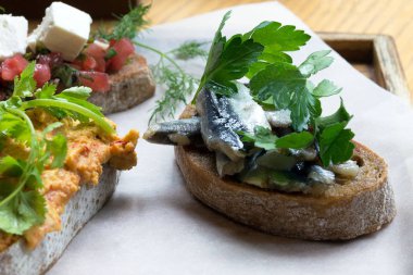 Farklı dolgular ile gevrek kızarmış ekmek. Beyaz bir fırın kağıdı üzerinde humus, tuzlu balık, domates, beyaz peynir ve otlar ile tost. Doyurucu bir atıştırmalık. Lezzetli sandviçler.