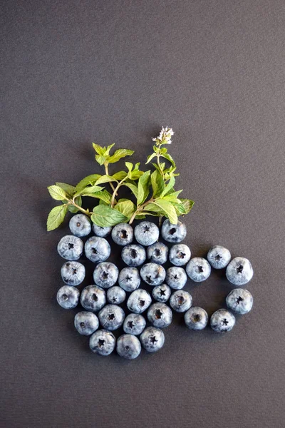 Grote smakelijke bosbessen en groene munt bladeren op een donkere achtergrond, aangelegd in de vorm van een beker. Gezonde bes. Vaccinium walstro. — Stockfoto