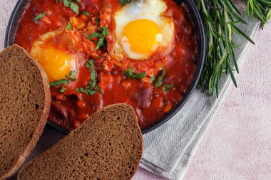 Shakshuka bir sos domates, acı biber, soğan ve baharatlar siyah bir dökme demir tava üzerinde kızarmış yumurta, lezzetli bir yemektir. Domates, pan, peçete ve parlak sabah güneş ışınlarının biberiye.
