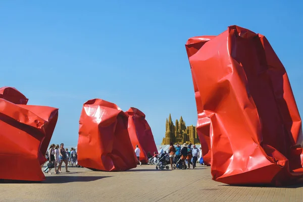 Ostend, Belgium, August 2019. People walk along the promenade of Ostend. Large red metal structures resembling crumpled bags. Belgium. Contemporary art in the open. An amusing trip. — Stock Photo, Image