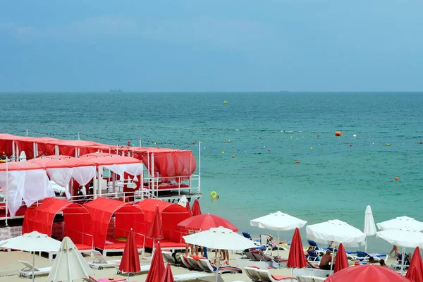 Odessa, Ukrayna, Haziran 2020. Karadeniz kıyısındaki plajda kırmızı bungalovlar ve şemsiyeler. İnsanlar Coronavirus 'tan sonra güneşlenip rahatlıyorlar. Ukrayna 'ya Seyahat.