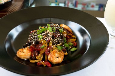 Lokantadaki siyah tabakta deniz ürünleri ve sebzeli ulusal Japon yemeği. Uzun kahverengi-gri buğday eriştesi. Yakın çekim..