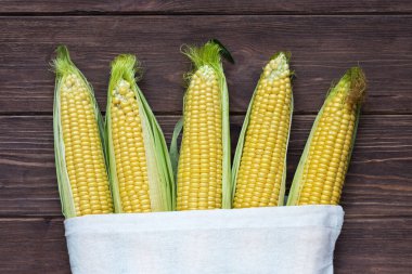 Koyu ahşap arka planda beyaz keten bir çantada koçandaki olgun mısır. Popüler tahıl ürünleri.