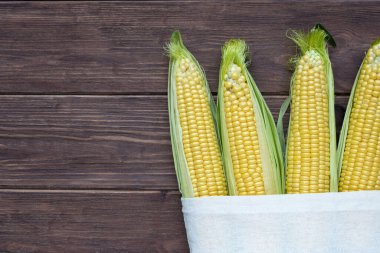 Koyu ahşap arka planda beyaz keten bir çantada koçandaki olgun mısır. Popüler tahıl ürünleri.
