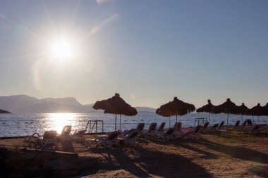 Gün batımında deniz kenarındaki şemsiyeler ve güneş şezlongları. Türkiye 'ye seyahat. Deniz kenarında dinlen..