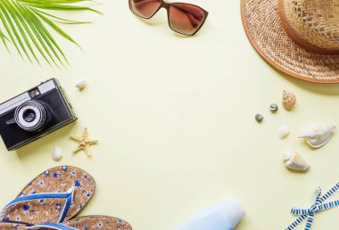 Seyahat Aksesuarları: sarı arka plan boşluk ile yeşil tropikal palmiye yaprağı, parmak arası terlik, fotoğraf makinesi, deniz ve güneş gözlüğü vardır. Üstten görünüm seyahat veya tatil kavramı, düz yatıyordu yaz arka plan