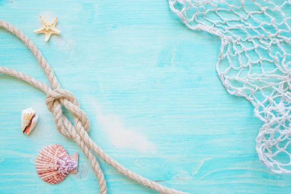Rough hemp rope tied knot sea, hells, starfishes and fishing network are on the background of blue faded wooden deck. Marine concept