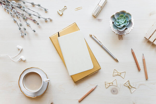 Female home office desk table in golden tones. Workspace with notebooks, cup of coffe and decorations on light wooden background with copy-space. Flat lay, top view