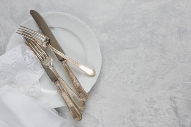 Bir porselen tabak ve Belçika dantel ile beyaz peçete üzerinde gümüş çatal bıçak takımı olan arka plan boşluk ile gri beton yüzey üzerinde