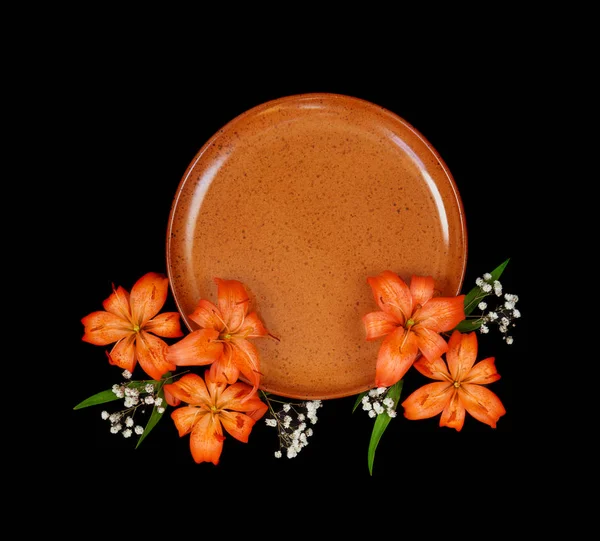 Beautiful orange lilies flowers and empty clay plate, isolated on a black background