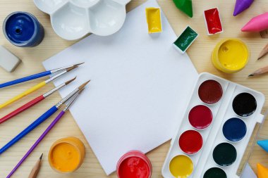 Sanat kavramı: fırçalar, boyalar ve palet bir ahşap arka plan, metin için yer ile çevrili küçük boş beyaz tuval ile kompozisyon