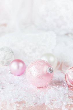 Beyaz ve pembe renklerde güzel Noel dekorasyonu: birkaç Noel topları beyaz kurdele ve inci bir ışık dantelli arka planda; boşluk ile dikey görüntü