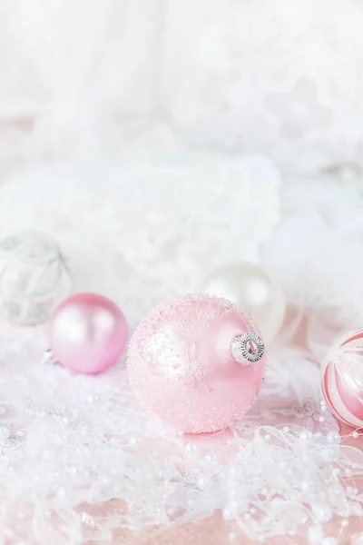 美丽的圣诞装饰白色和粉红色的颜色 几个圣诞球与白色丝带和珍珠在一个轻花边背景 具有复制空间的垂直图像 — 图库照片