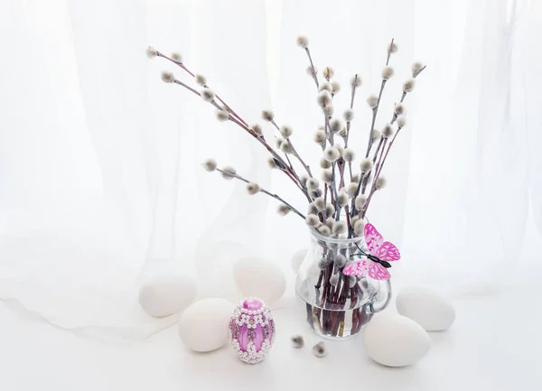 复活节贺卡 蓬松的小柳树树枝在透明的玻璃水罐 粉红色的面蛇和白色结束粉红色的复活节彩蛋对白色透明的布 — 图库照片