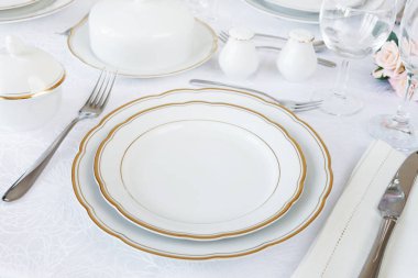 Tablo boş beyaz tabaklar, gözlük, çatal bıçak takımı ve lüks masa örtüsü çiçekler ile dekore edilmiş