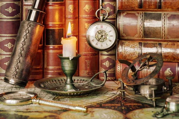 复古概念的发现 旅客配件 古董望远镜 放大镜 日记本 指南针 怀表和燃烧的蜡烛在一个古老的烛台的背景是在古董书籍的背景 — 图库照片