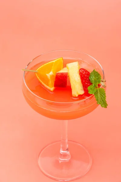 カラフルなフルーツパンチカクテルドリンクでクーペガラス上サンゴピンクの背景 — ストック写真