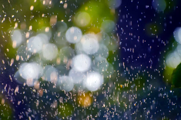 Summer rain falling over a natural blurred background of green leaves, soft focus bokeh lights and blue sky. Natural defocused background, perfect for creative designs.