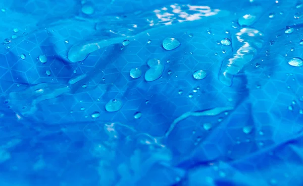 Nylon waterproof fabric background. Texture of blue woven synthetic waterproof clothing with water flowing on it