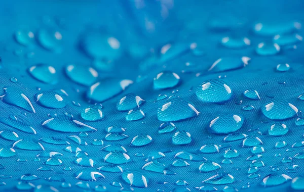 Water drops on waterproof nylon fabric. Macro detail view of texture of blue woven synthetic waterproof clothing. Waterproof fabric with waterdrops. Rain Drops on Water Resistant Textile waterproof coating background with water drops