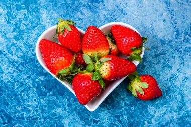 mavi bir arka plan üzerinde bir kalp şeklinde beyaz bir tabak içinde olgun çilek