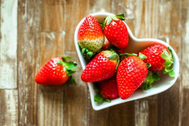  ahşap masa arka plan karşı bir kalp şeklinde beyaz bir tabak içinde çilek