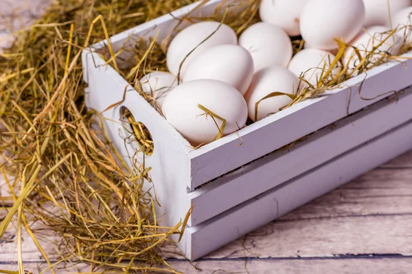 Eggs in a white wooden box with hay. Wooden background