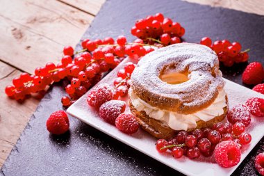 Kremalı pasta ve ahududu kırmızı böğürtlen ve ahşap bir masada frenk üzümü. Tatlı.
