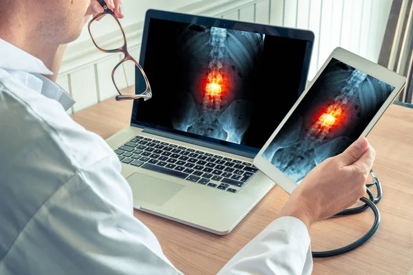 Doktor röntgen omurga ağrısı bir dizüstü bilgisayar ve dijital tablet ile izlemek