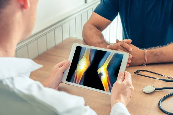 Doktor hastanın dizlerinin röntgenini çektiren dijital bir tablet tutuyor. Bacaklarda ağrı