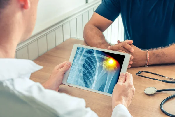 Doktor hastanın göğsünün röntgenini çektiren dijital bir tablet tutuyor. Omuzda ağrı