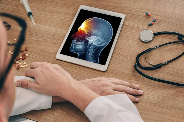 Doktor başının önünde bir ağrı ile kafatası x-ray ile dijital bir tablet izliyor