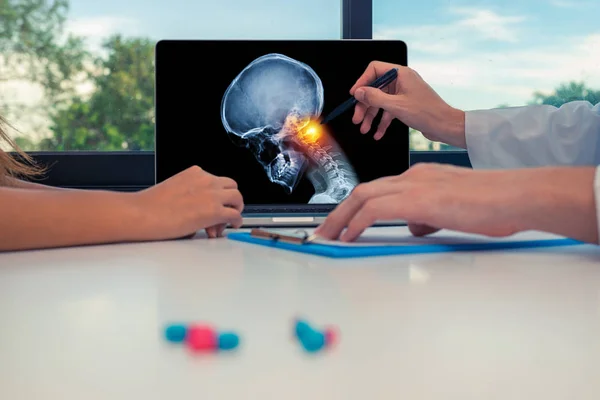 Doktor, bir kadın hastaya dizüstü bilgisayarda boynunun üst kısmında ağrı olan kafatasının röntgenini gösteriyor. Baş ağrısı migren veya travma kavramı
