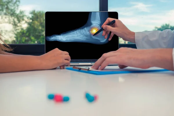 Doktor bir kadın hastaya dizüstü bilgisayarda ayak bileğinde bir ayak ve ağrı bir x-ray gösteren. Masada tıp