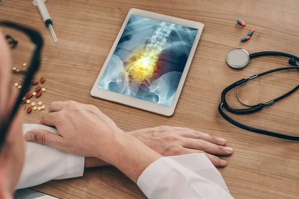 Doktor ağrı ile kalça ve omurga röntgeni ile dijital tablet izliyor