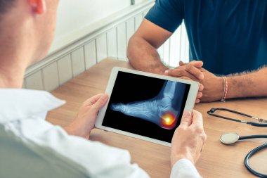 Doktor hastanın ayağının röntgenini çektirerek dijital bir tablet tutuyor. Topuk ağrısı
