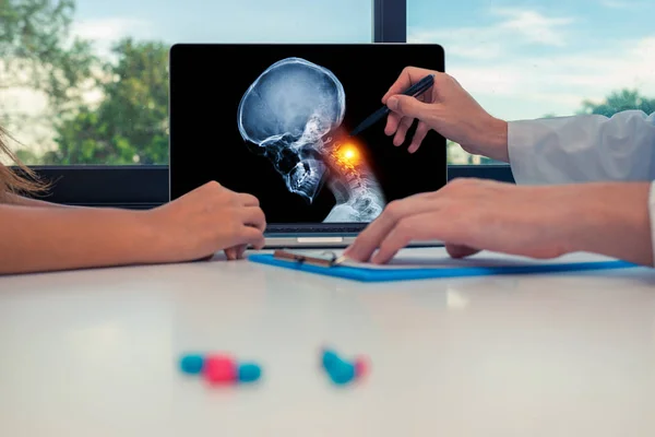 Doctor met een x-ray van de schedel met pijn in de nek op een laptop aan een vrouw patiënt. Hoofdpijn migraine of trauma concept — Stockfoto