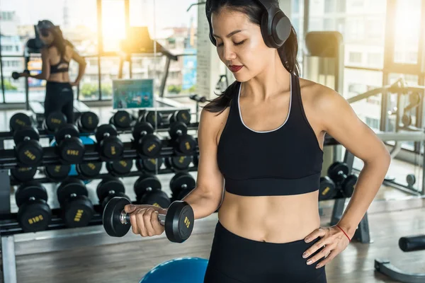 Mujer asiática entrenando brazos en el gimnasio con pesas mientras escucha música con auriculares — Foto de Stock