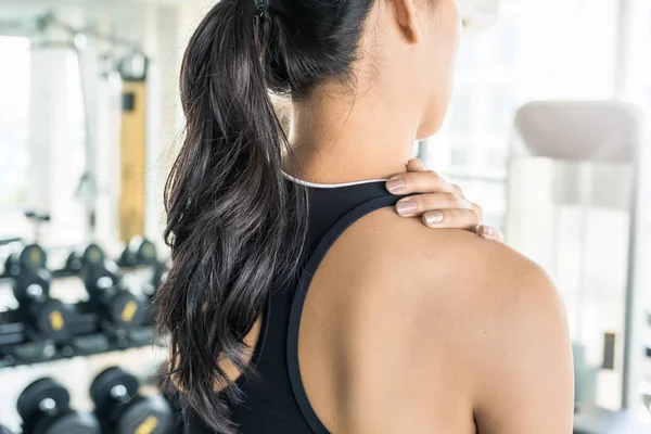 Mujer asiática sosteniendo su cuello en el gimnasio. Lesiones en el hombro o espalda durante el entrenamiento — Foto de Stock