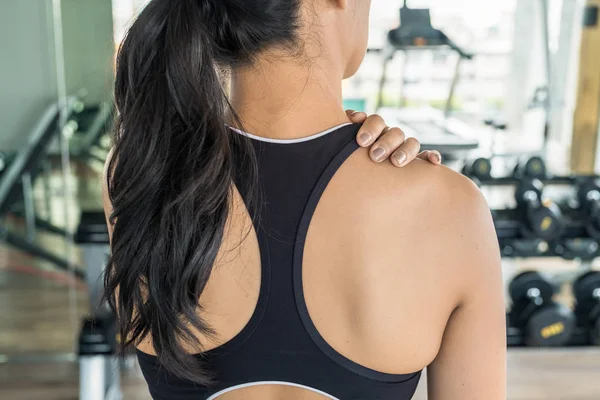 Mujer asiática sosteniendo su hombro en el gimnasio. Lesiones en el hombro o espalda durante el entrenamiento — Foto de Stock