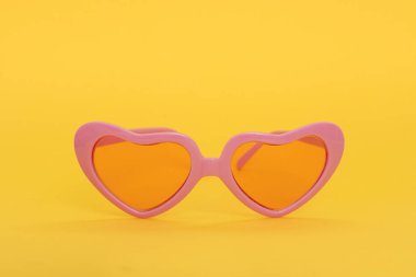Pembe kalp şeklinde sarı bir arka plan üzerinde güneş gözlüğü
