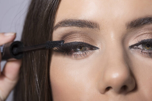 Young brunette woman putting mascara on eyelashes
